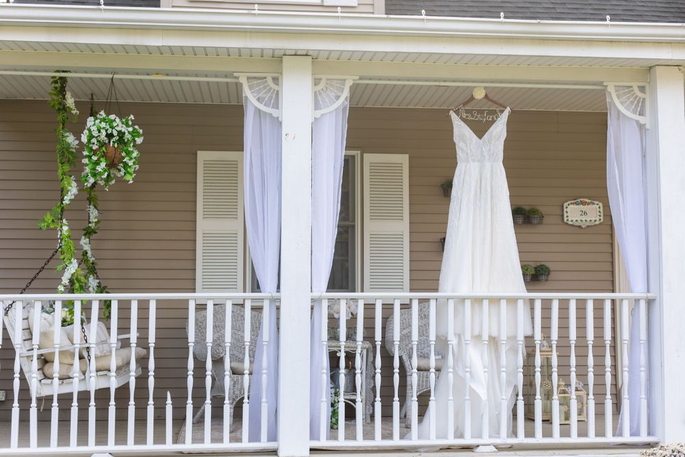 Elegant white wedding dress displayed on front porch of classic house.