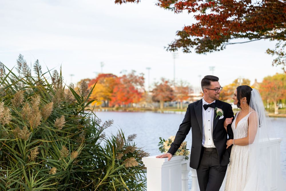 Autumn wedding portrait by lake with fall foliage in background.
