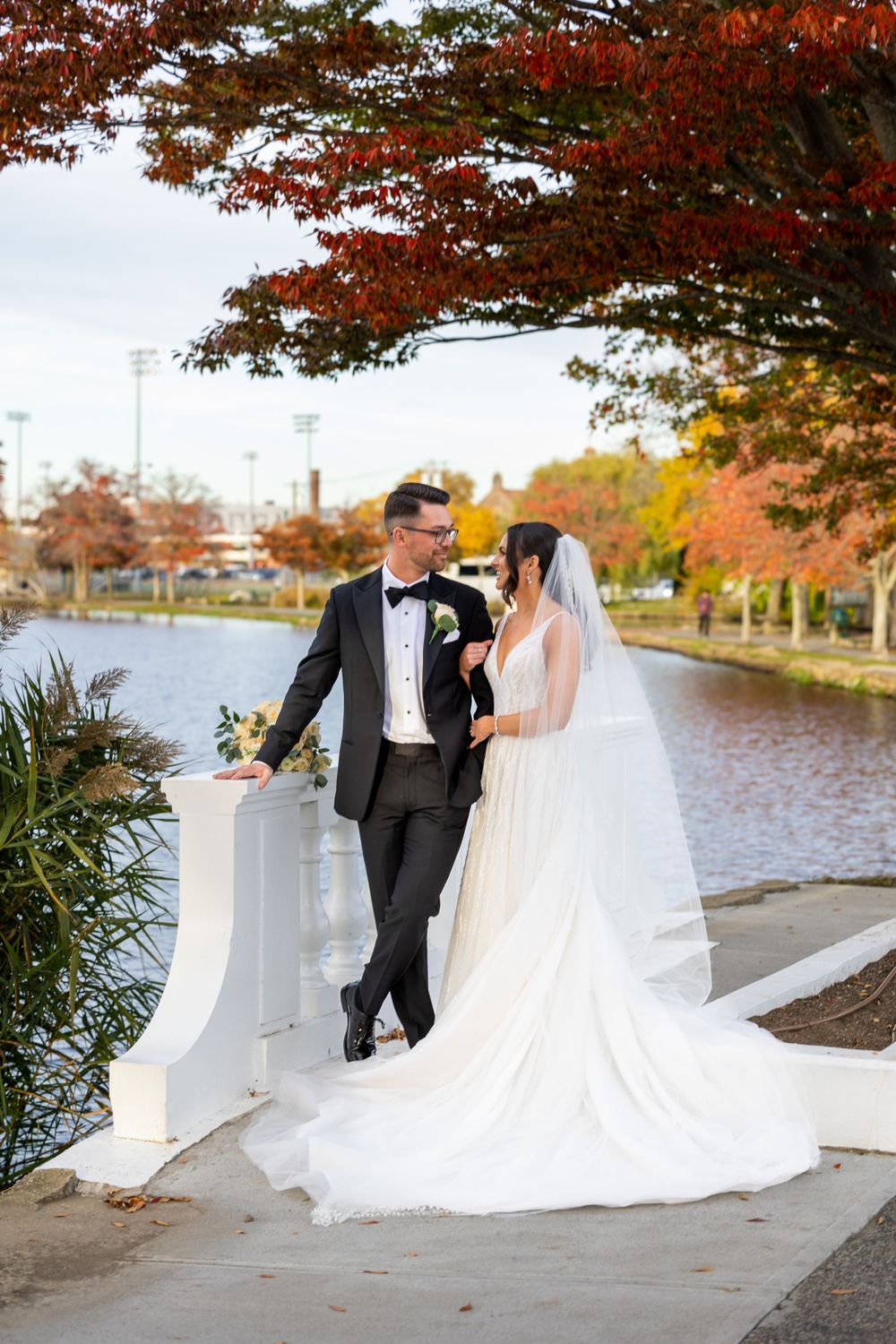 Couple posing on white bridge with dramatic fall colors and lake in background.