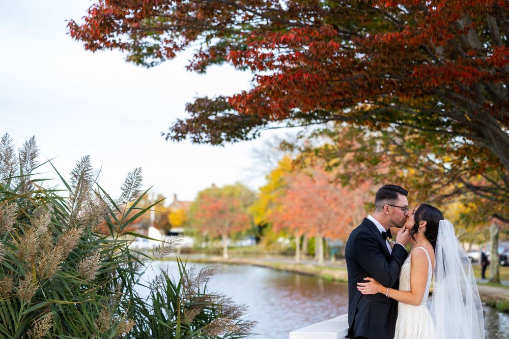 Wedding couple shares an intimate moment under red autumn leaves by a serene waterway.