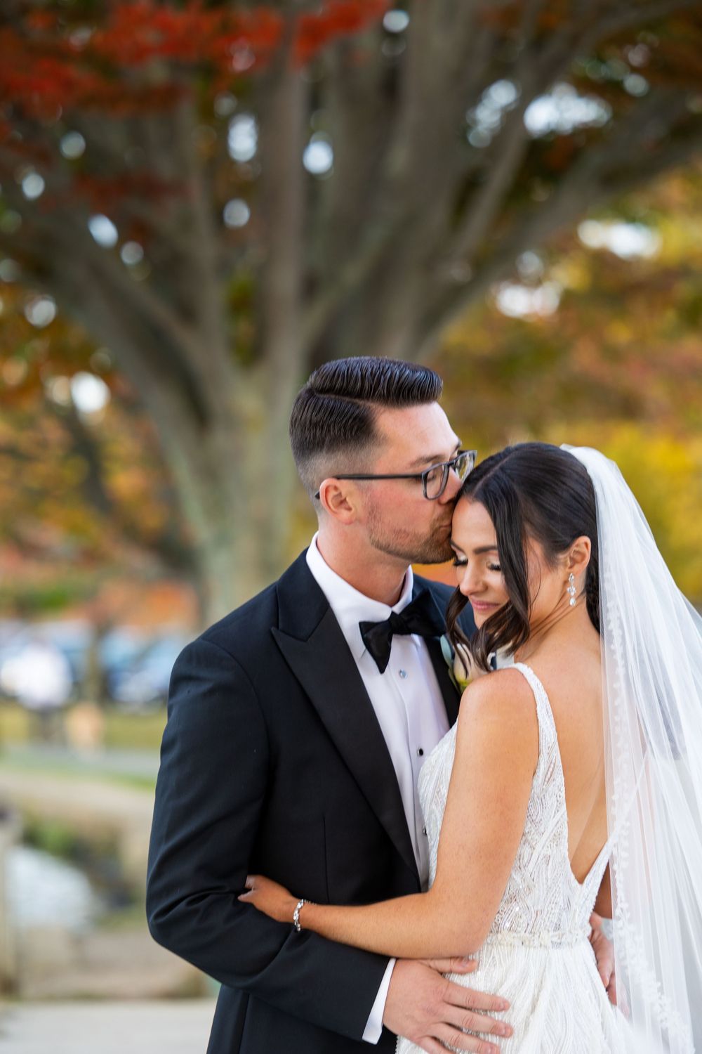 Close-up of newlyweds sharing a tender moment under a fall tree with bokeh background.