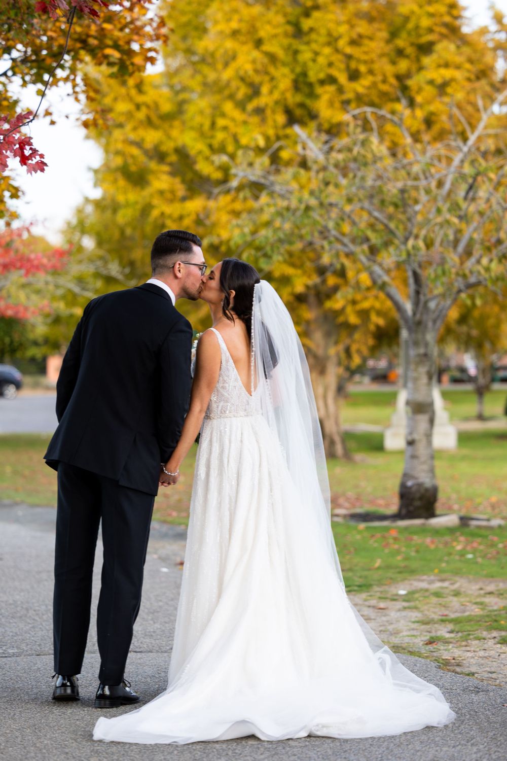 Back view of newlyweds walking together under colorful autumn trees.