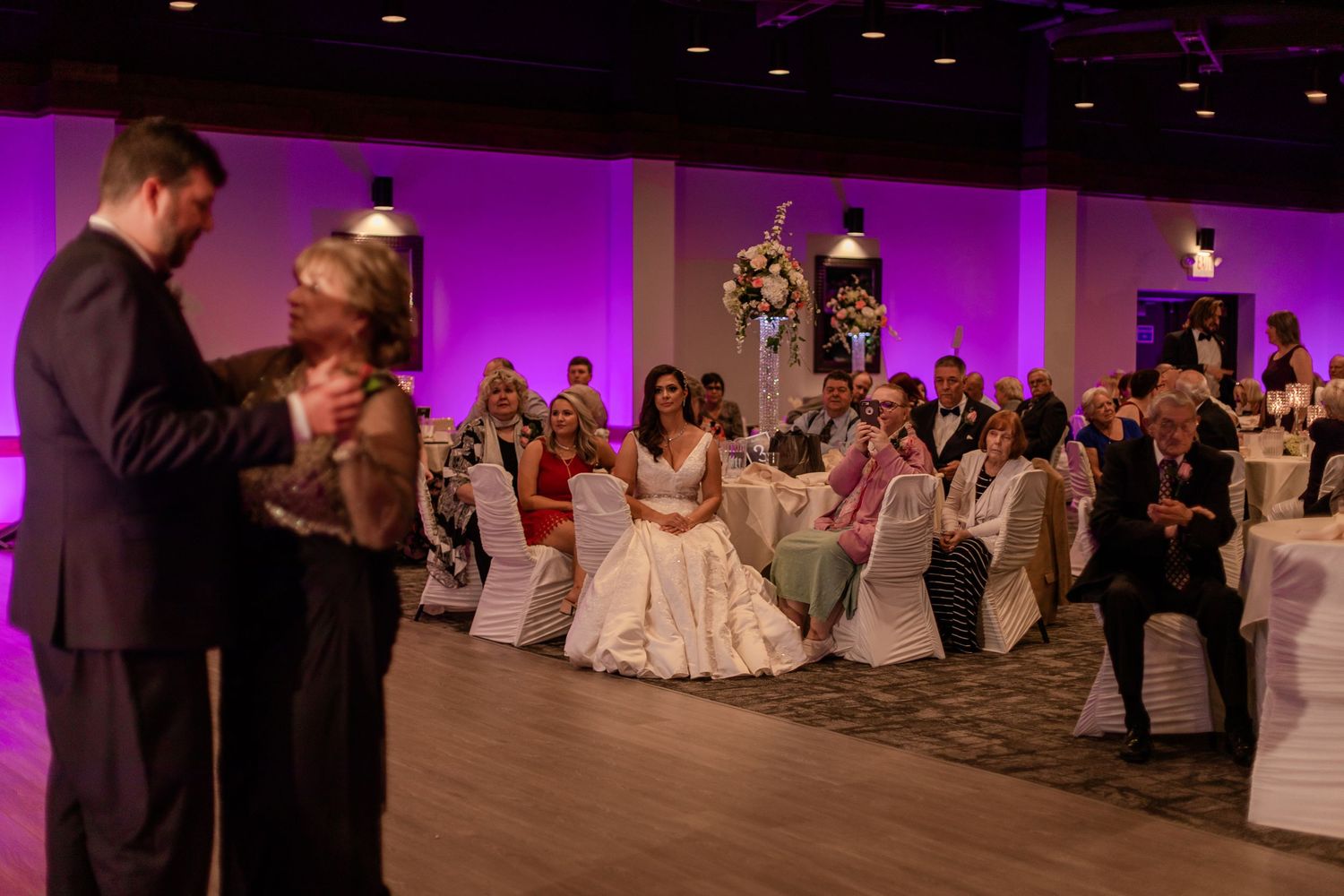 Wedding reception dance floor scene with purple lighting and white chair covers.