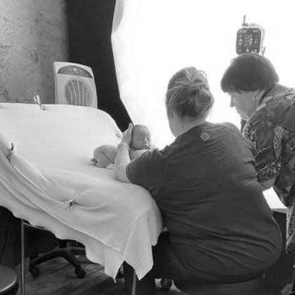 Black and white image showing individuals gathered around a medical examination bed.