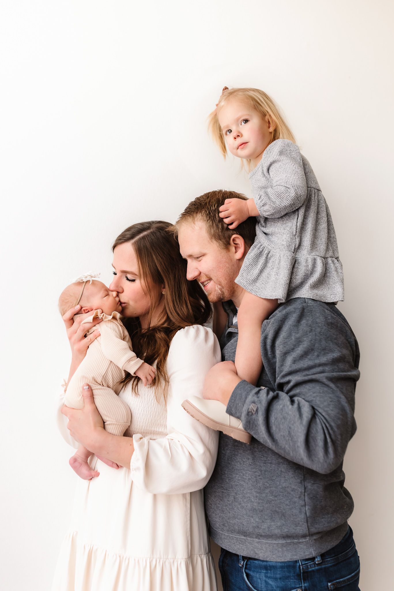 Intimate family photography session with parents and children in casual wear against white background.