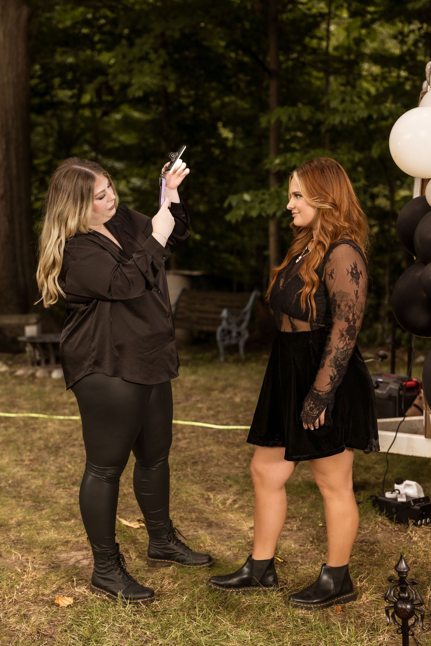 Two friends in black outfits chat outdoors during a Halloween-themed event.