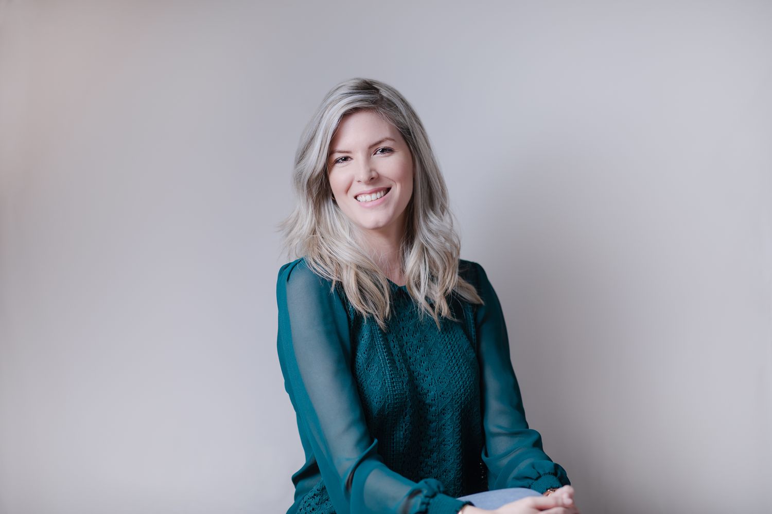 Portrait of a woman in teal sheer blouse sitting against neutral background.