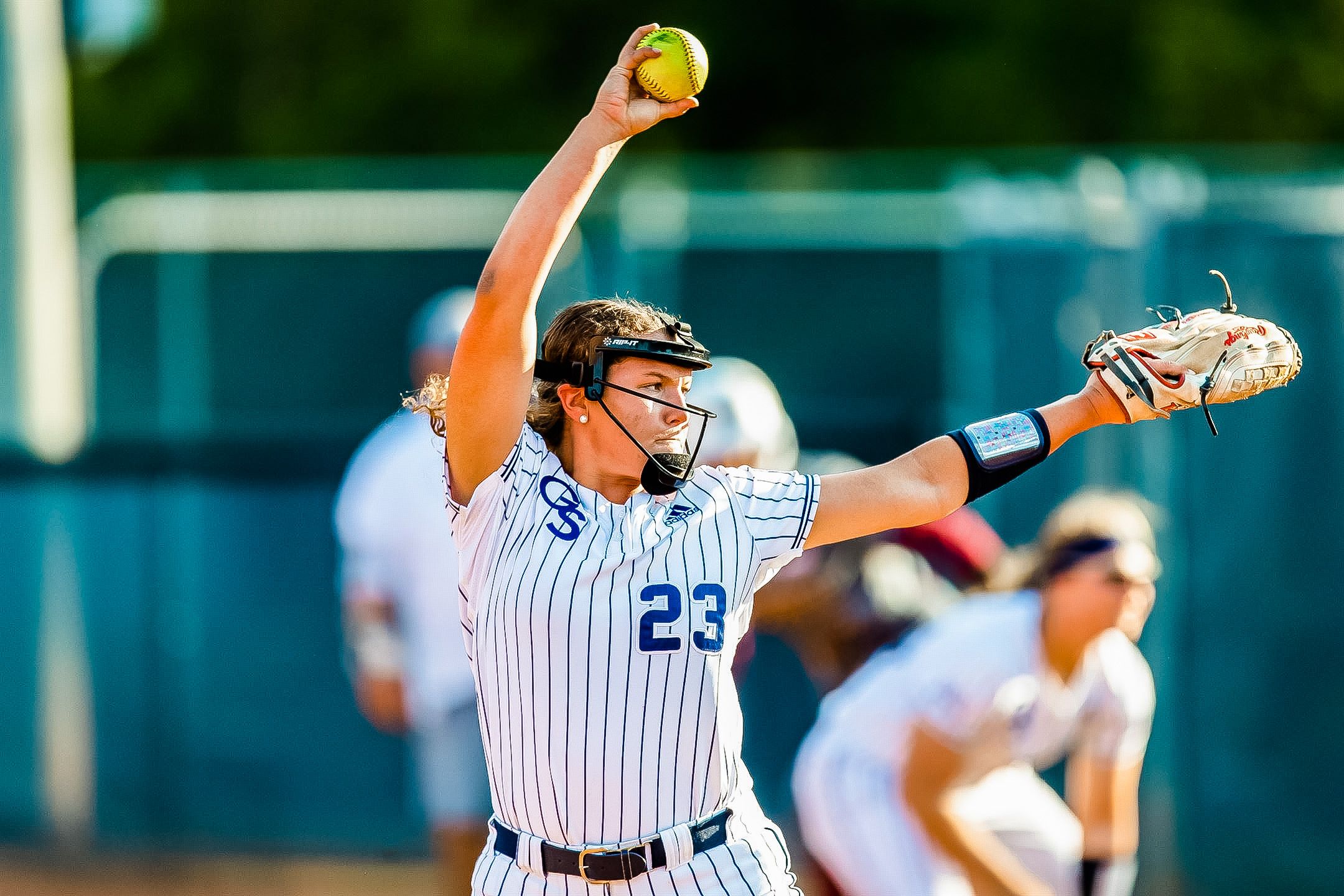 Softball pitcher in pinstripe uniform throws pitch during game.