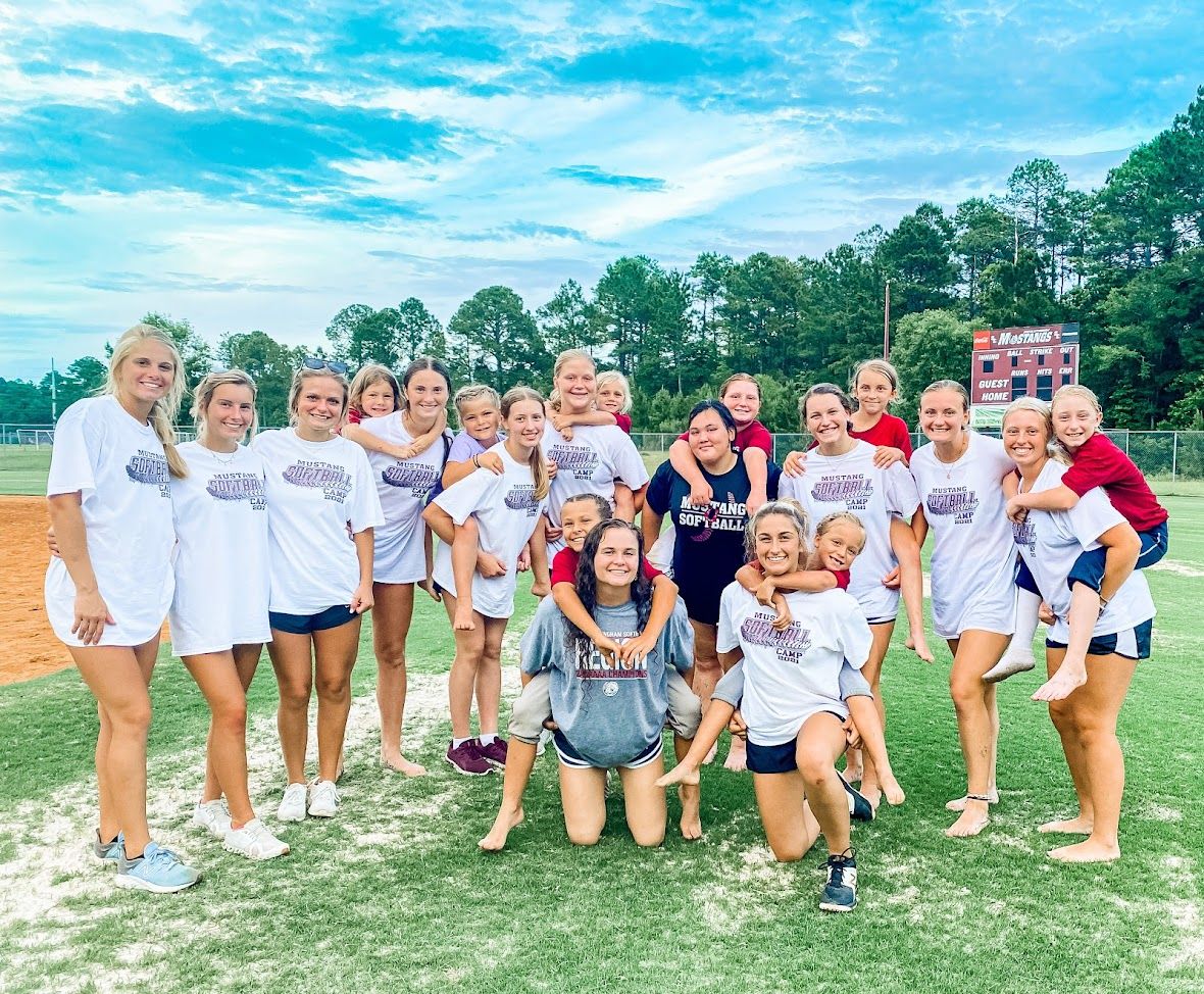 Team photo of softball players posing together on a sunny field.