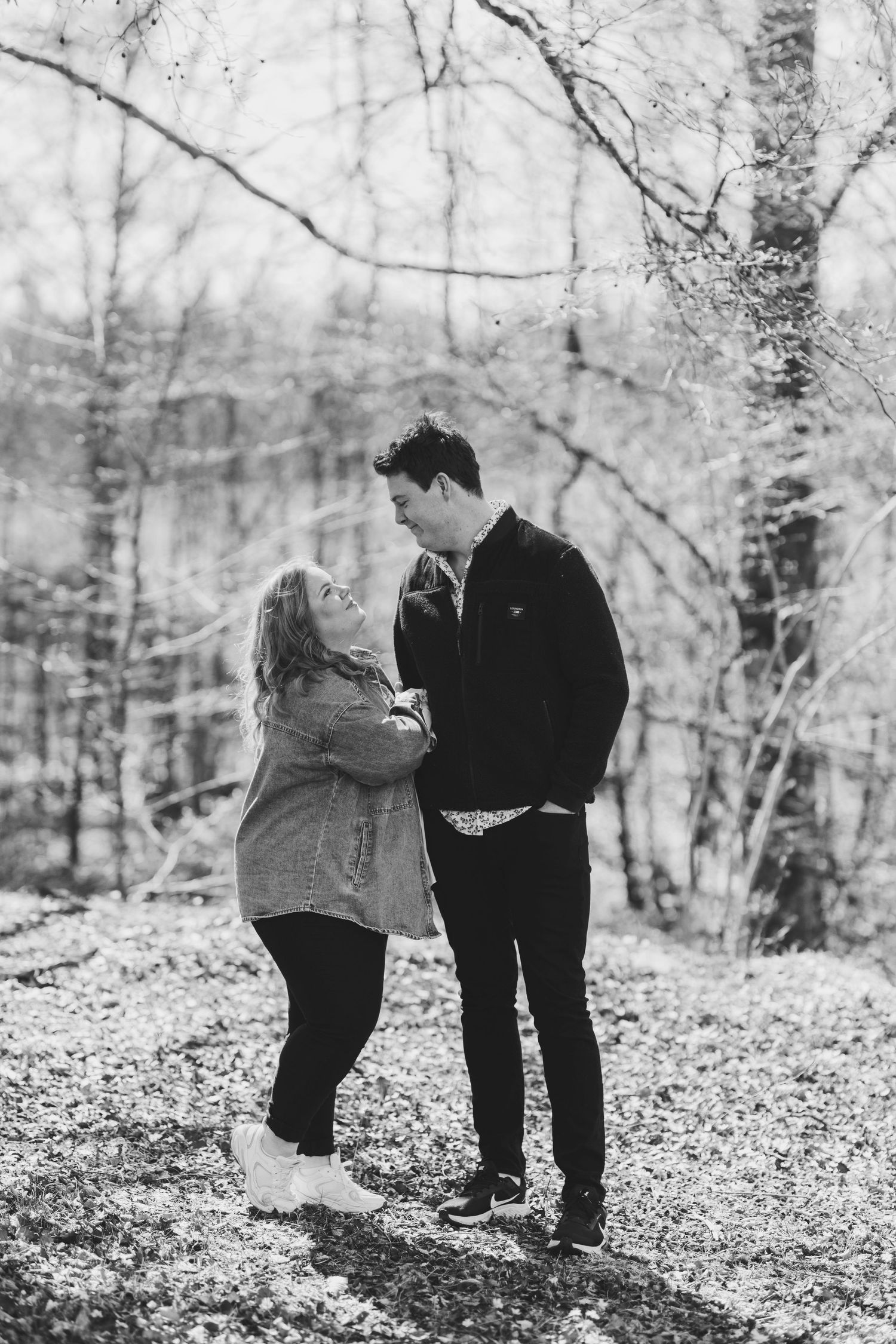Black and white photo of couple laughing together in winter forest setting.