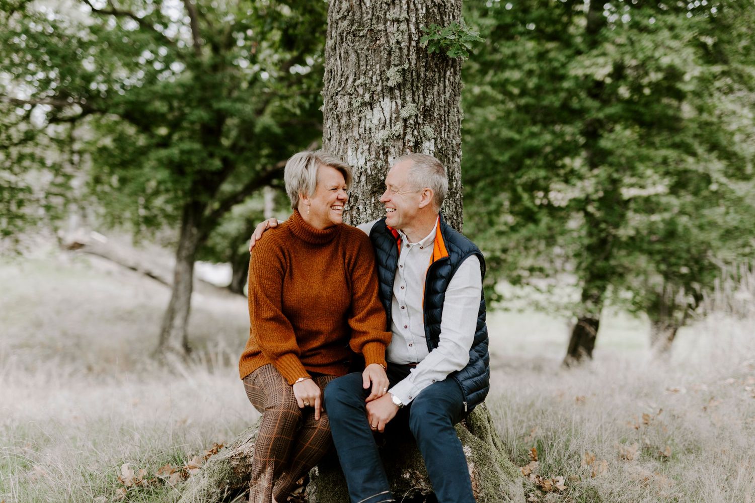 Mature couple sitting together on tree trunk in serene woodland setting.