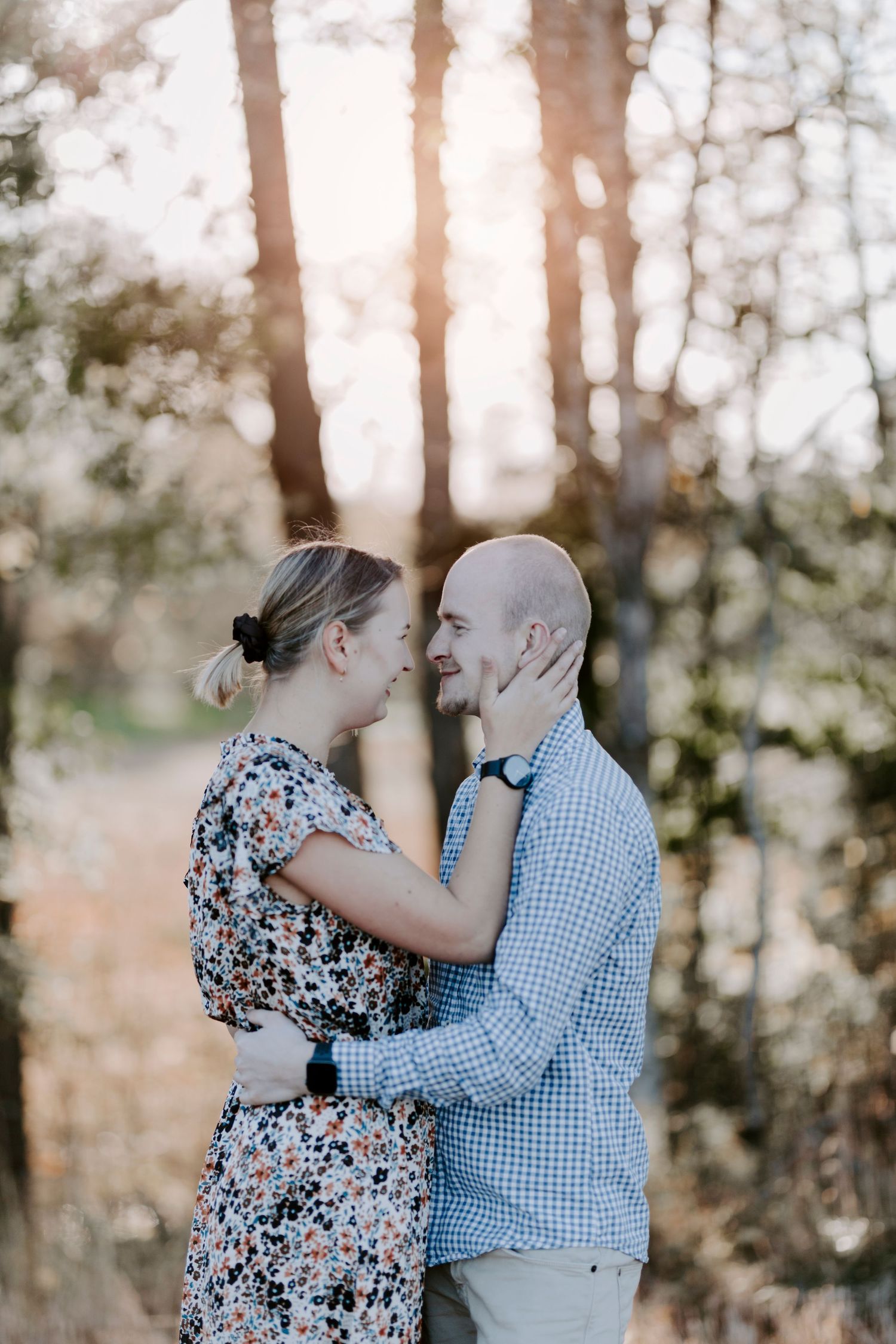 Intimate couple embracing in forest with sunset light filtering through trees.