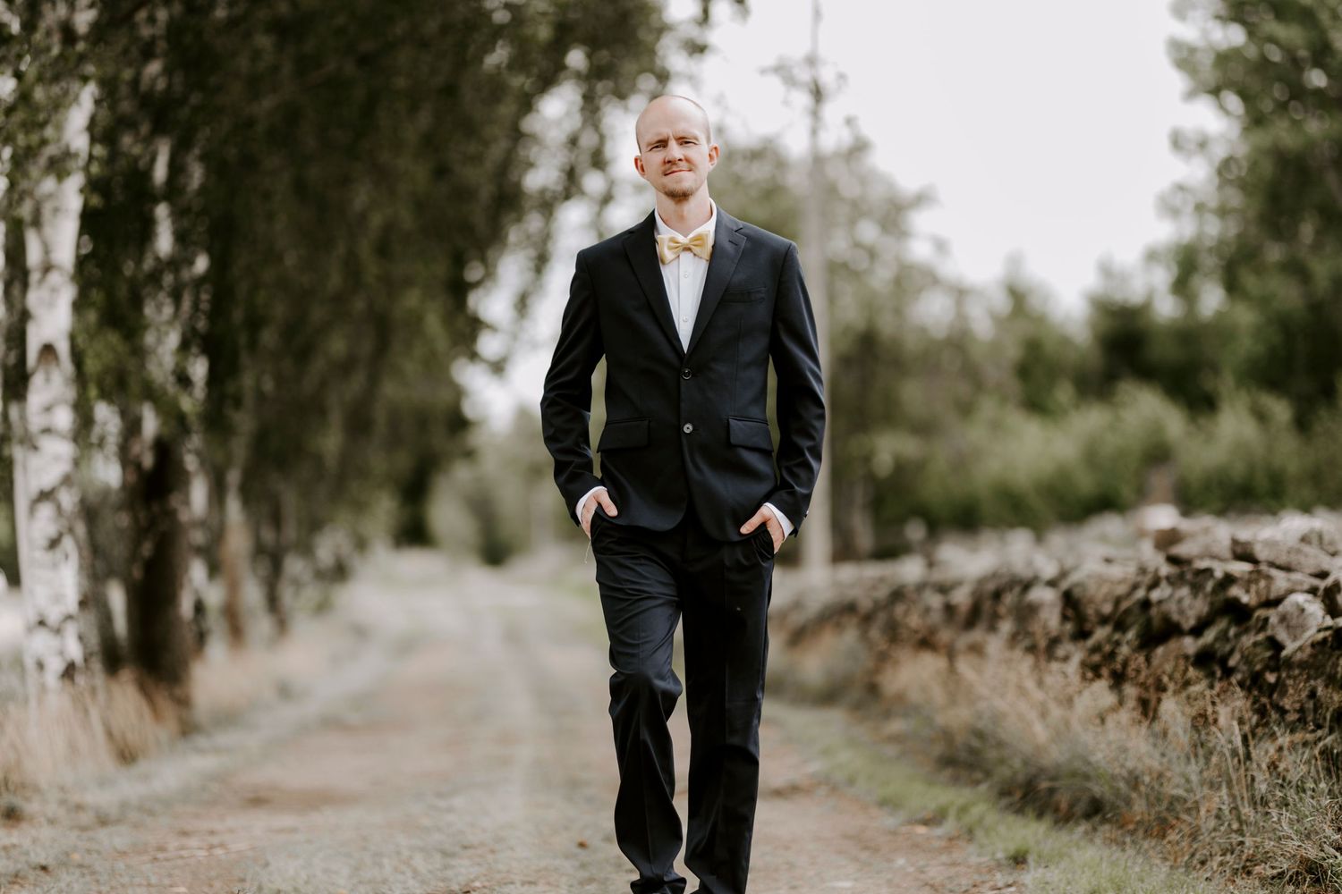 Professional portrait of person in dark suit standing on countryside path.