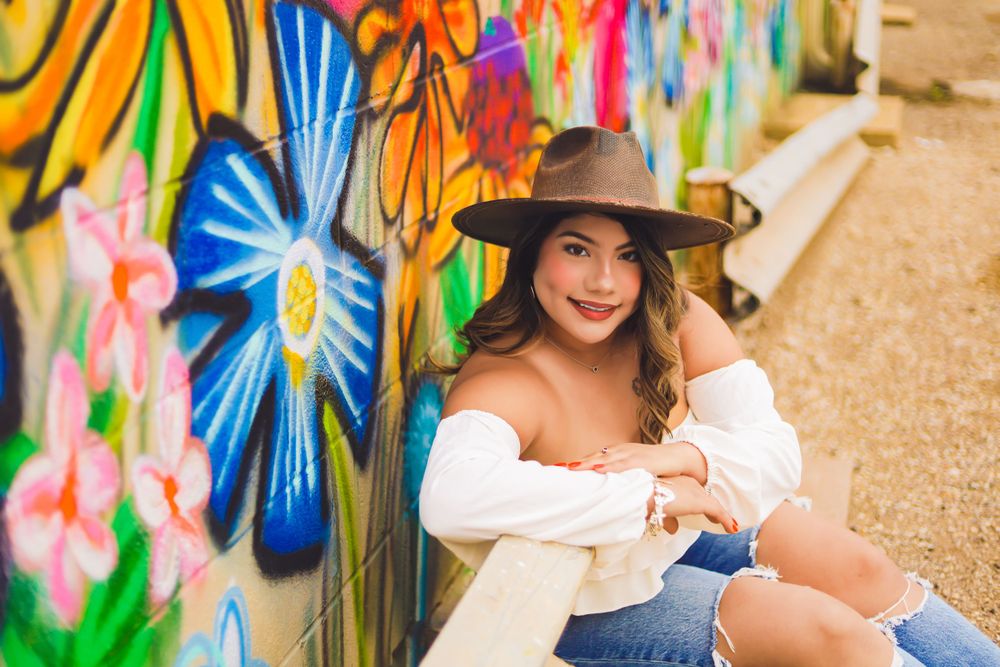 A portrait against a vibrant graffiti wall featuring bright floral designs and an off-shoulder white top.