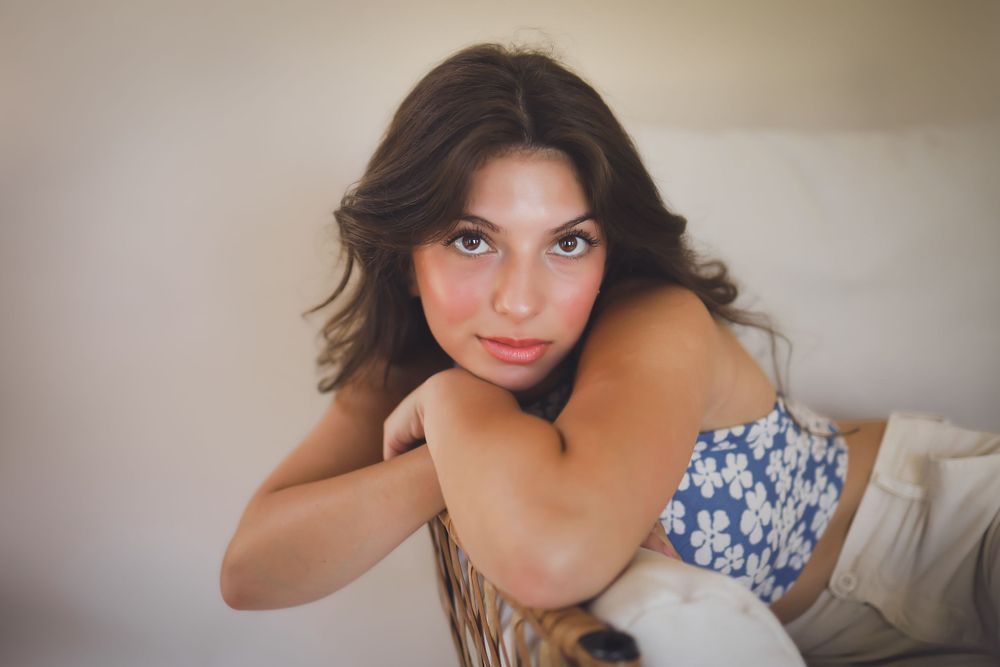 Portrait of woman in floral top resting head on arm against light background.