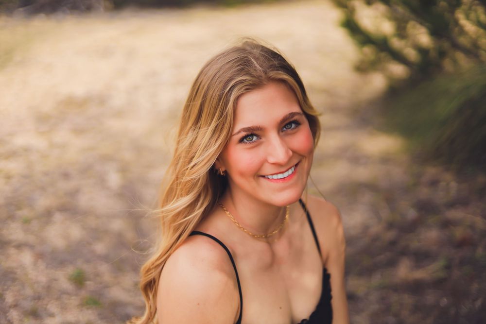 Natural outdoor portrait of woman with long hair smiling warmly at camera.