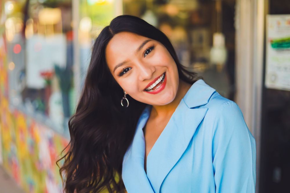 Professional headshot of woman in light blue blazer smiling against colorful background.