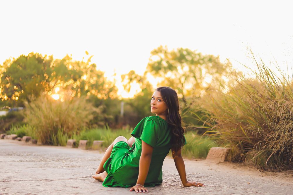 Woman in flowing green dress sits on sandy ground during sunset.