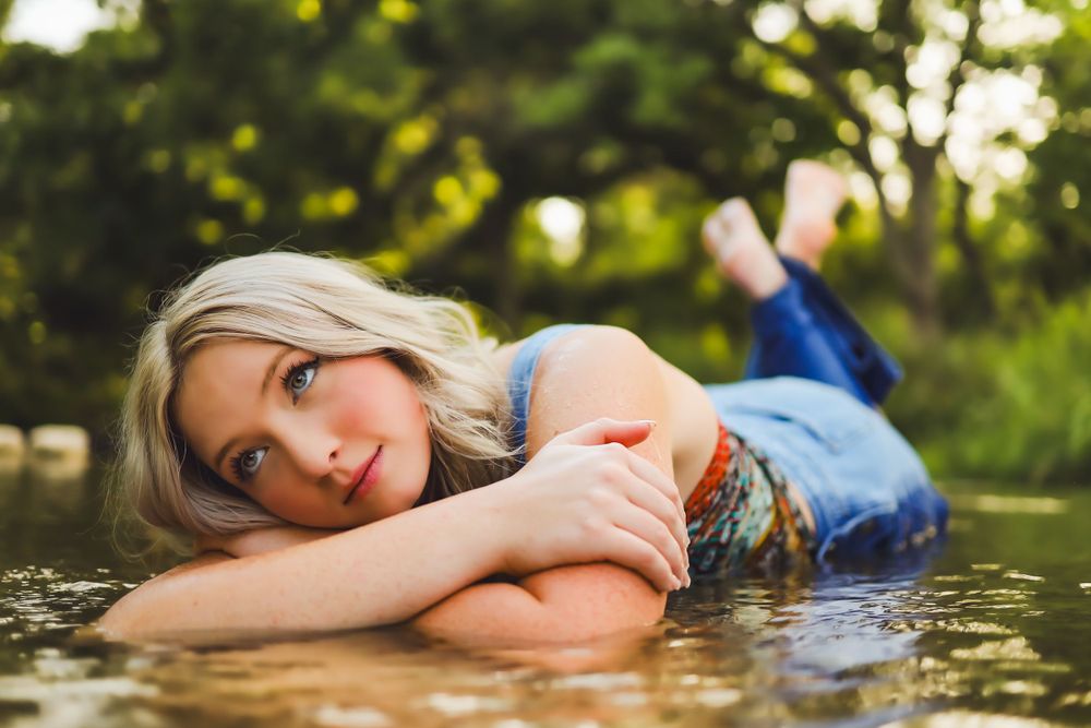 A creative outdoor portrait lying near water with natural sunlight filtering through trees.