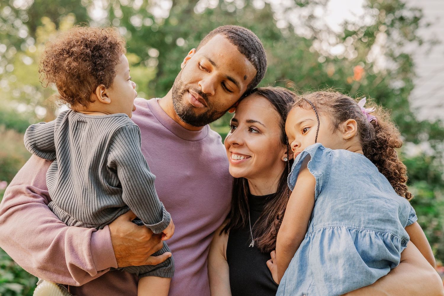 A joyful family moment captured outdoors with two children being held by their parents in a garden setting.