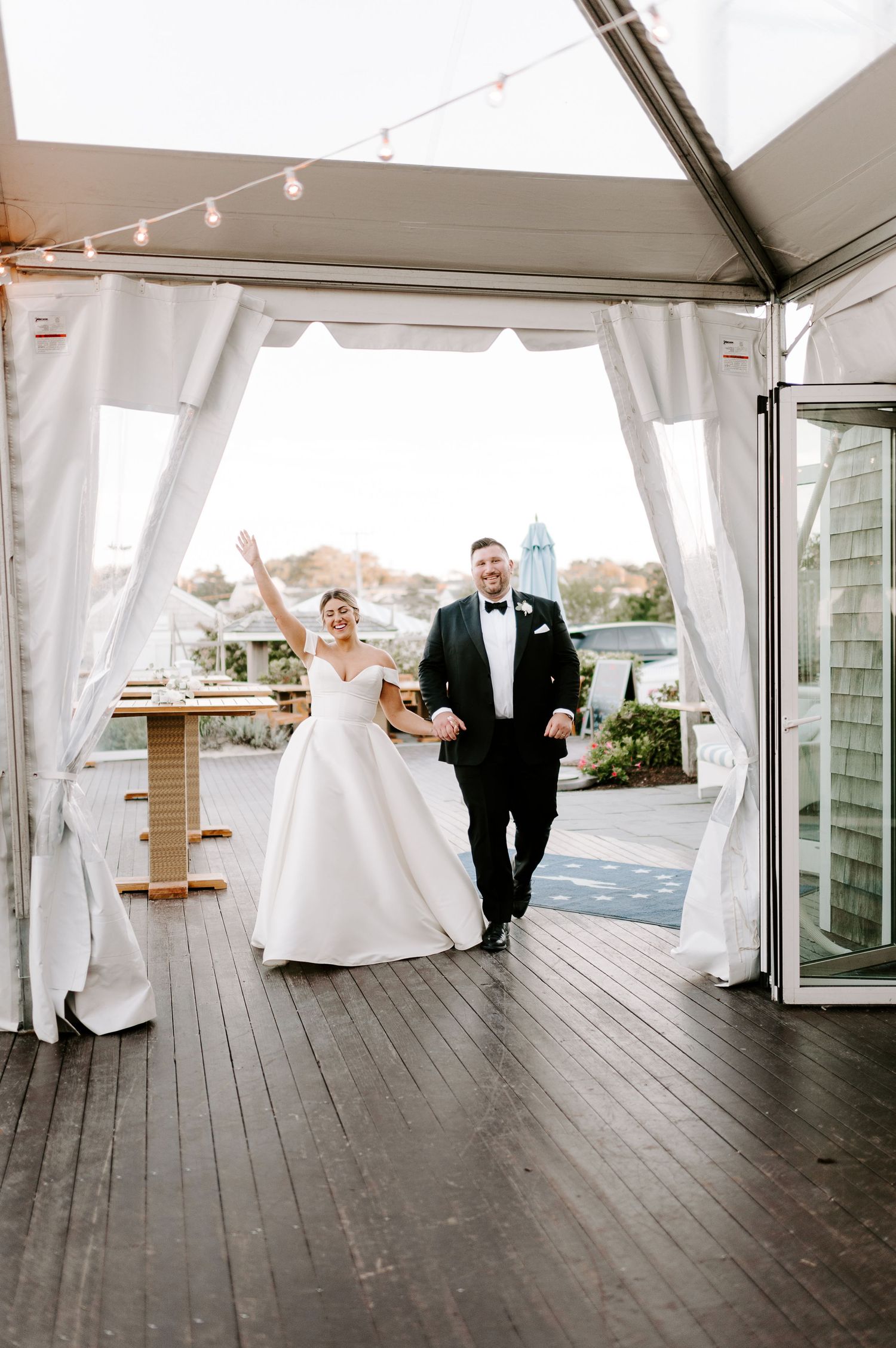 Wedding couple dances and celebrates under a white tent structure with wooden flooring.