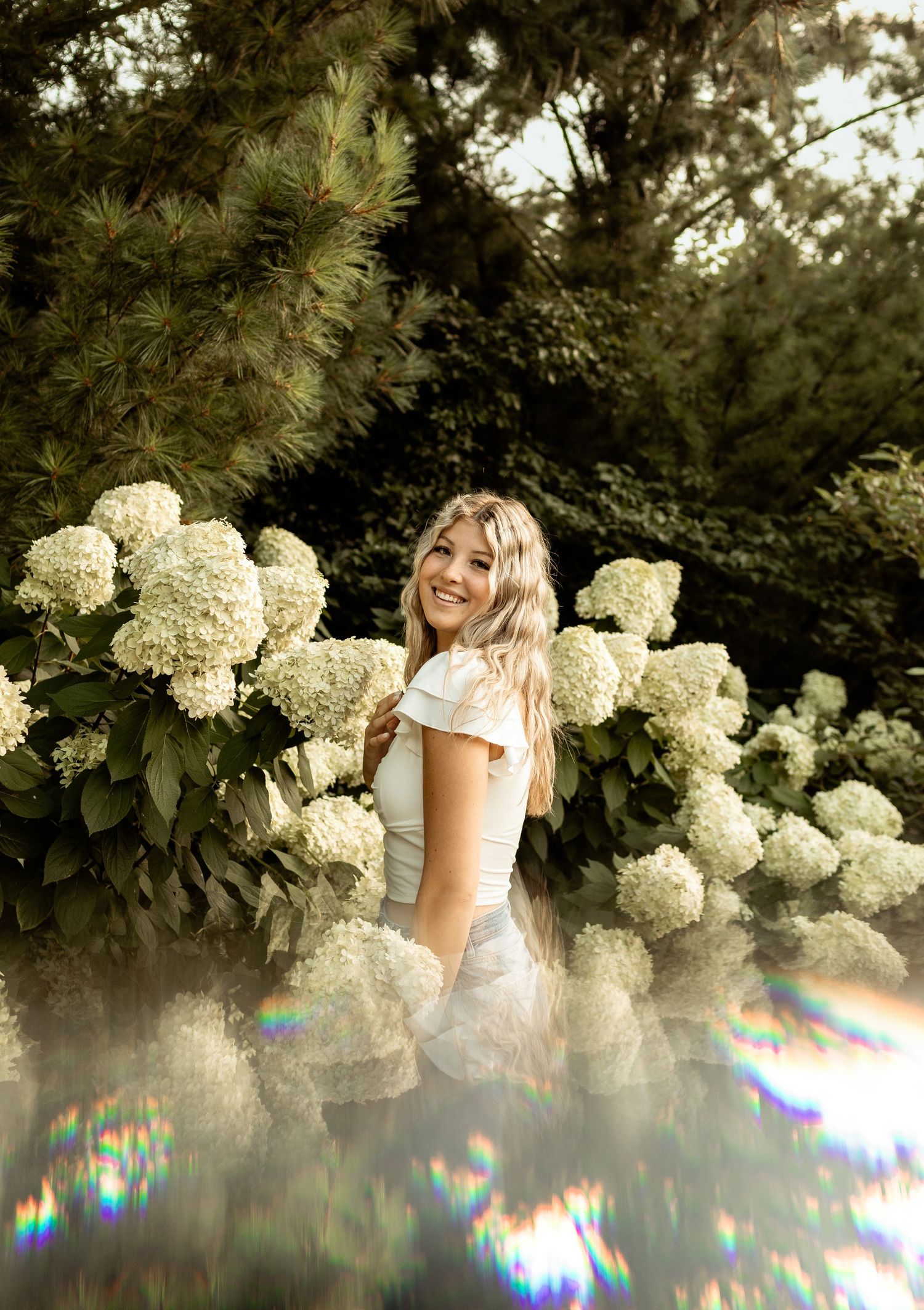Portrait in garden with white hydrangea flowers and rainbow lens flares.