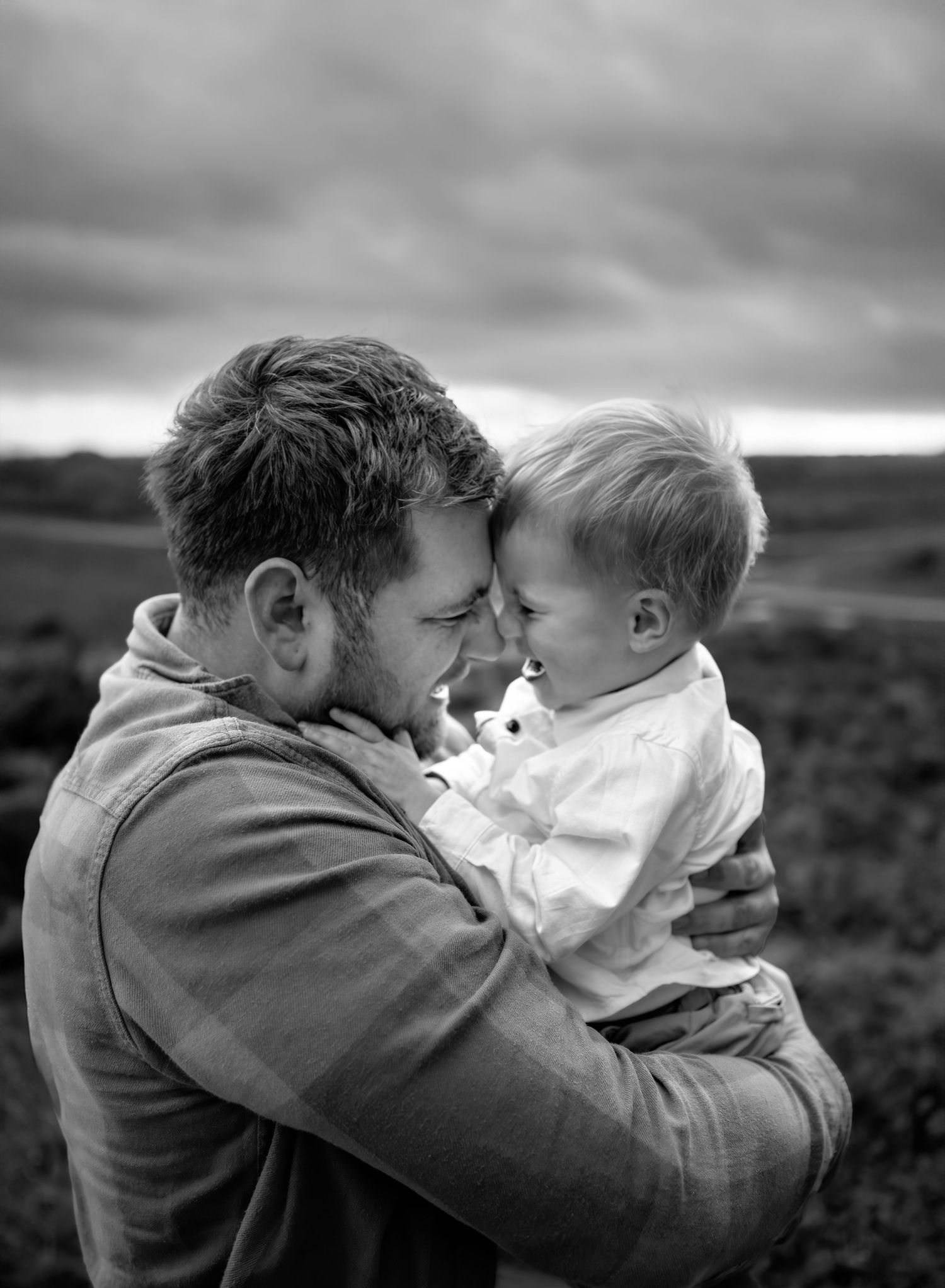 Dad and son touching heads and smiling. Black and white photo. Family photo session in the New Forest, Lymington.