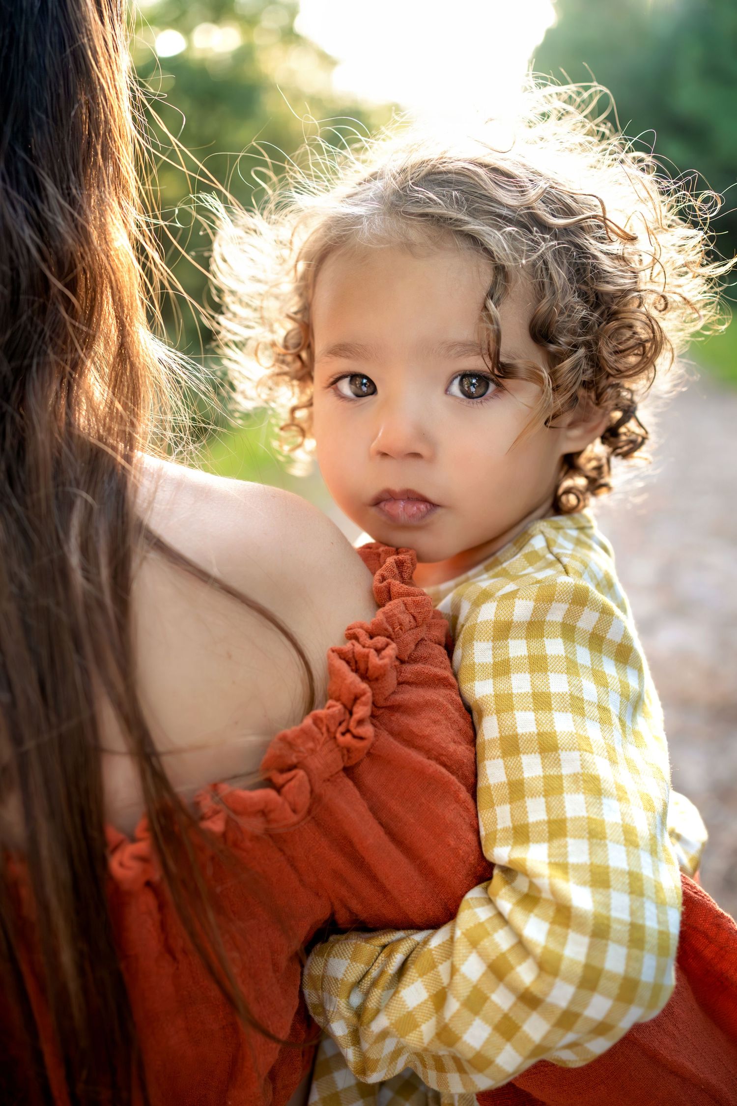 Curly-haired toddler, in mother's arms at sunset. Family photo session in the New Forest, Lymington, Hampshire.