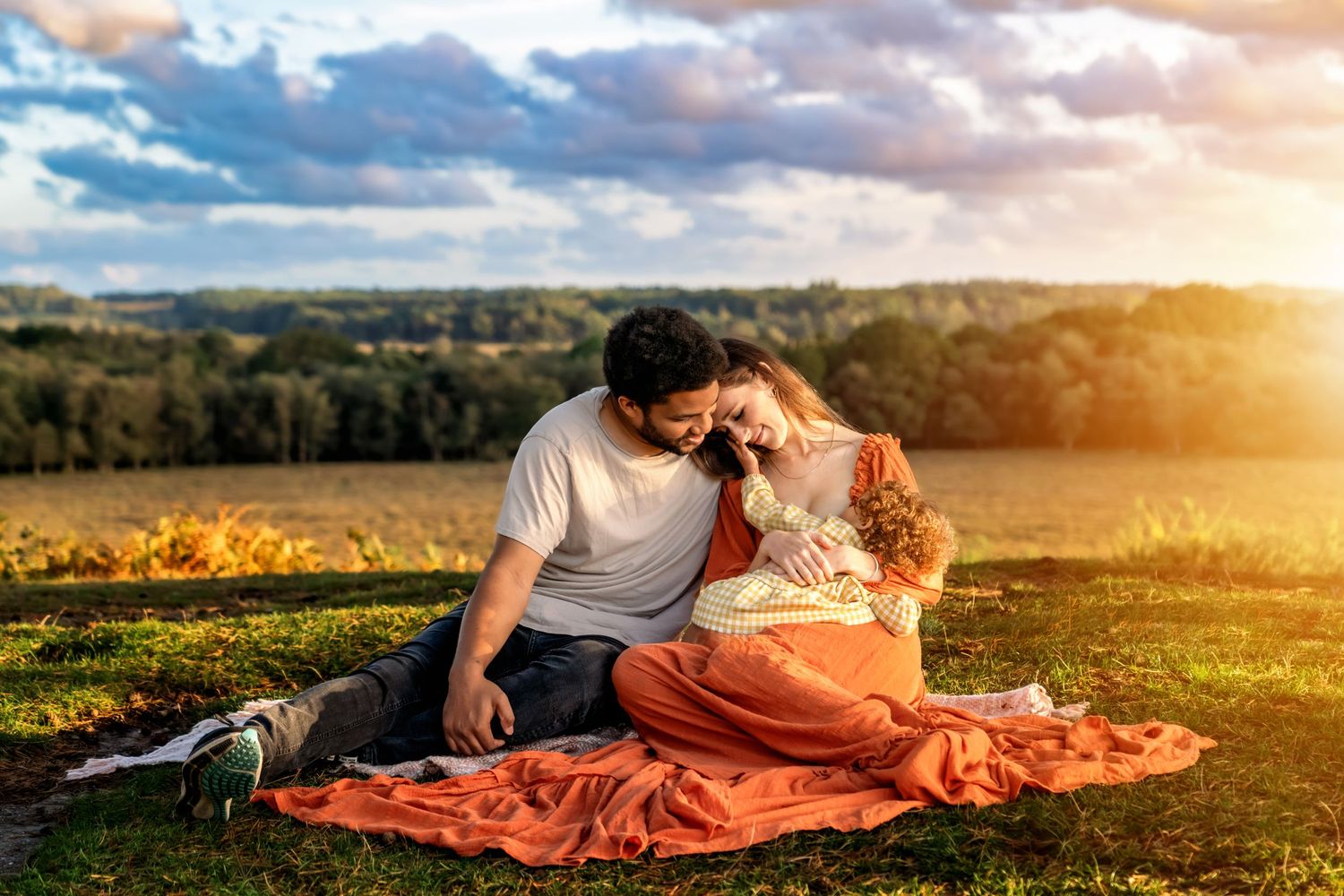 Mother and father loving the baby, sitting on a blanket watching the sunset in the New Forest, Hampshire.