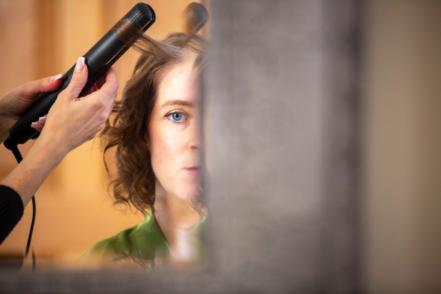 Hair styling session captured through a mirror reflection with soft lighting.