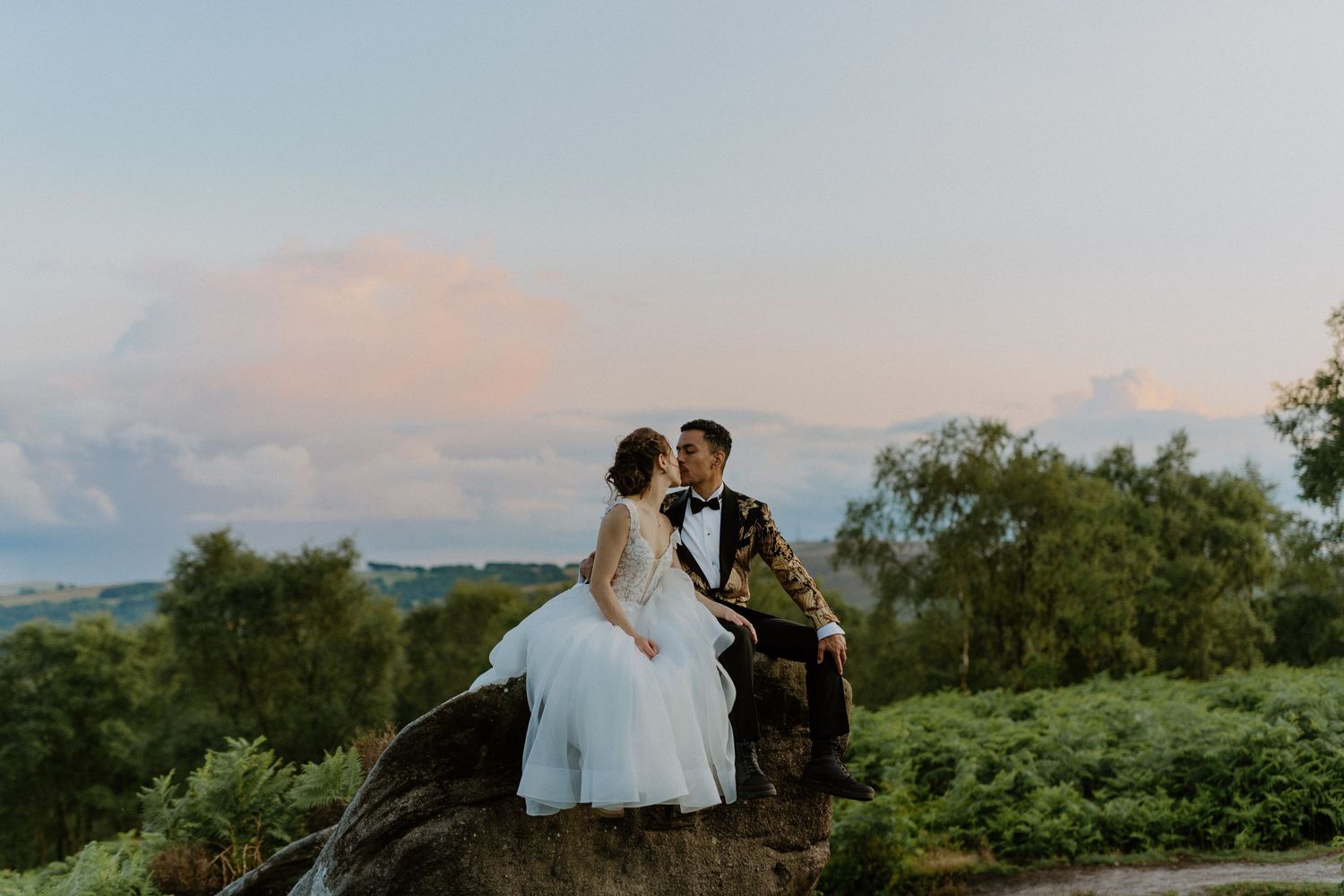 Romantic sunset wedding portrait of couple sitting on rocky overlook.