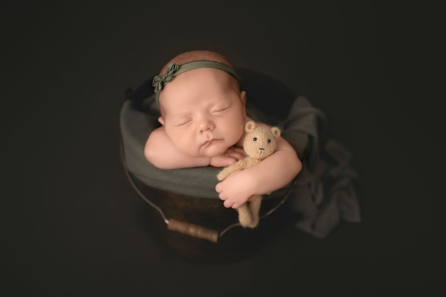 Sleeping newborn in dark setting hugging small teddy bear with soft fabric details.