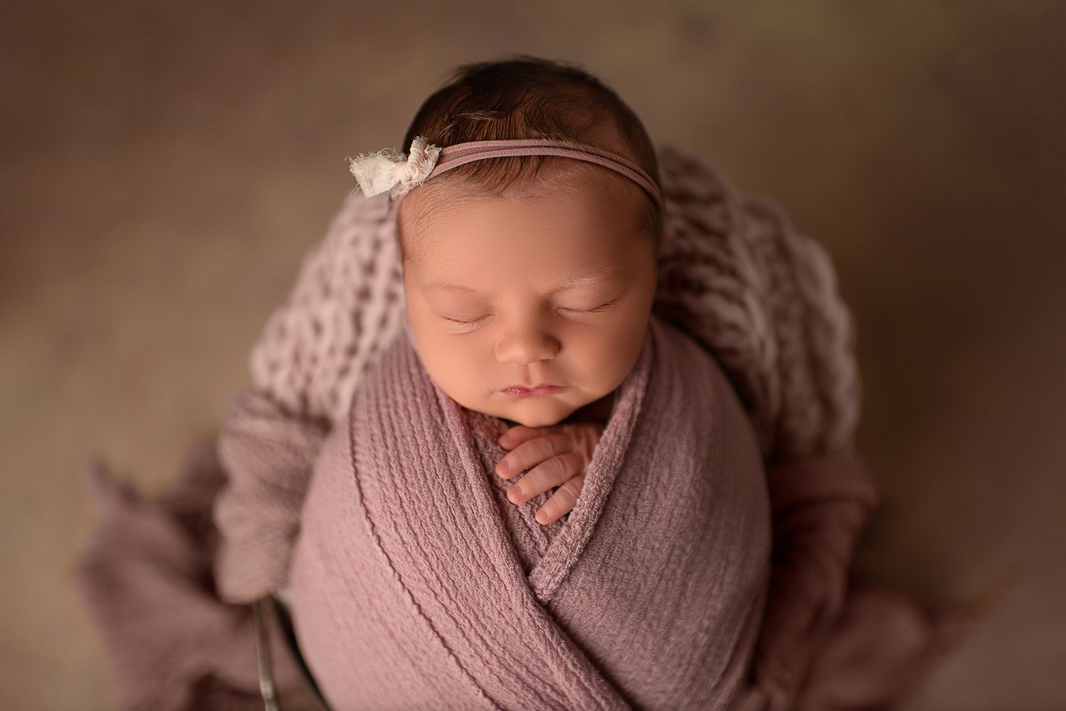 Peaceful sleeping newborn wrapped in soft pink knit wrap with delicate headband.