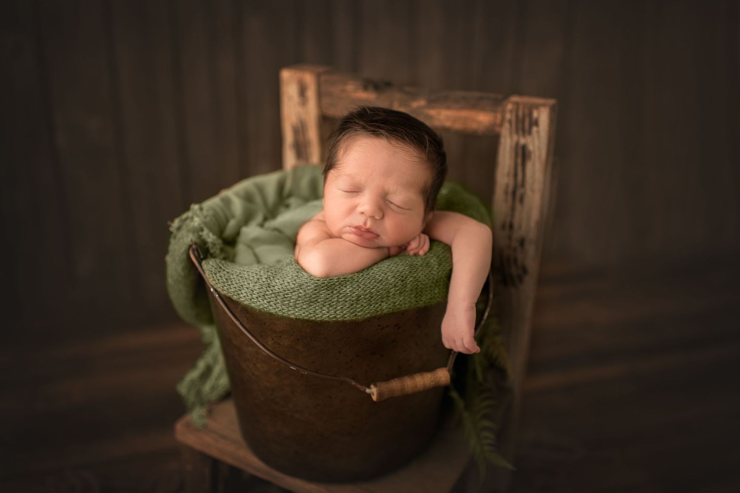 Newborn sleeping in vintage wooden bucket with green textured fabric.