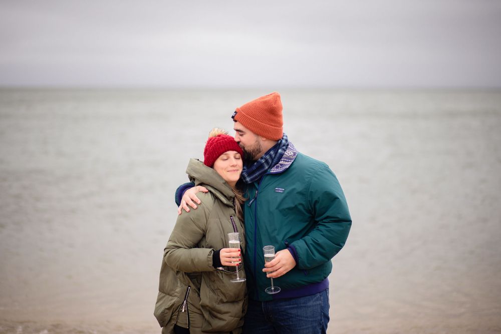 Couple sharing an intimate moment on a foggy beach wearing winter coats and beanies.