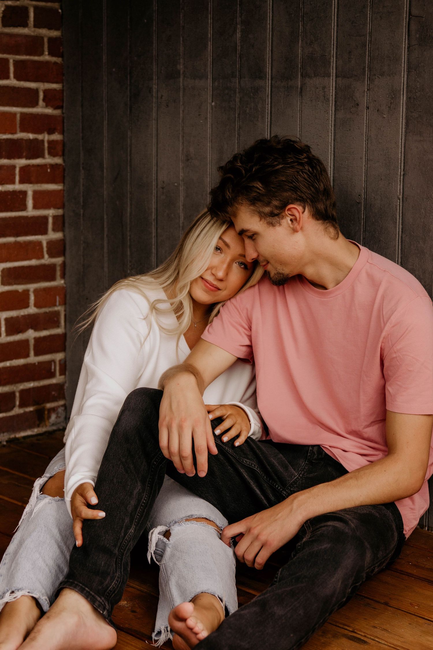 Romantic couple sitting together on wooden floor, woman resting head on mans shoulder tenderly.