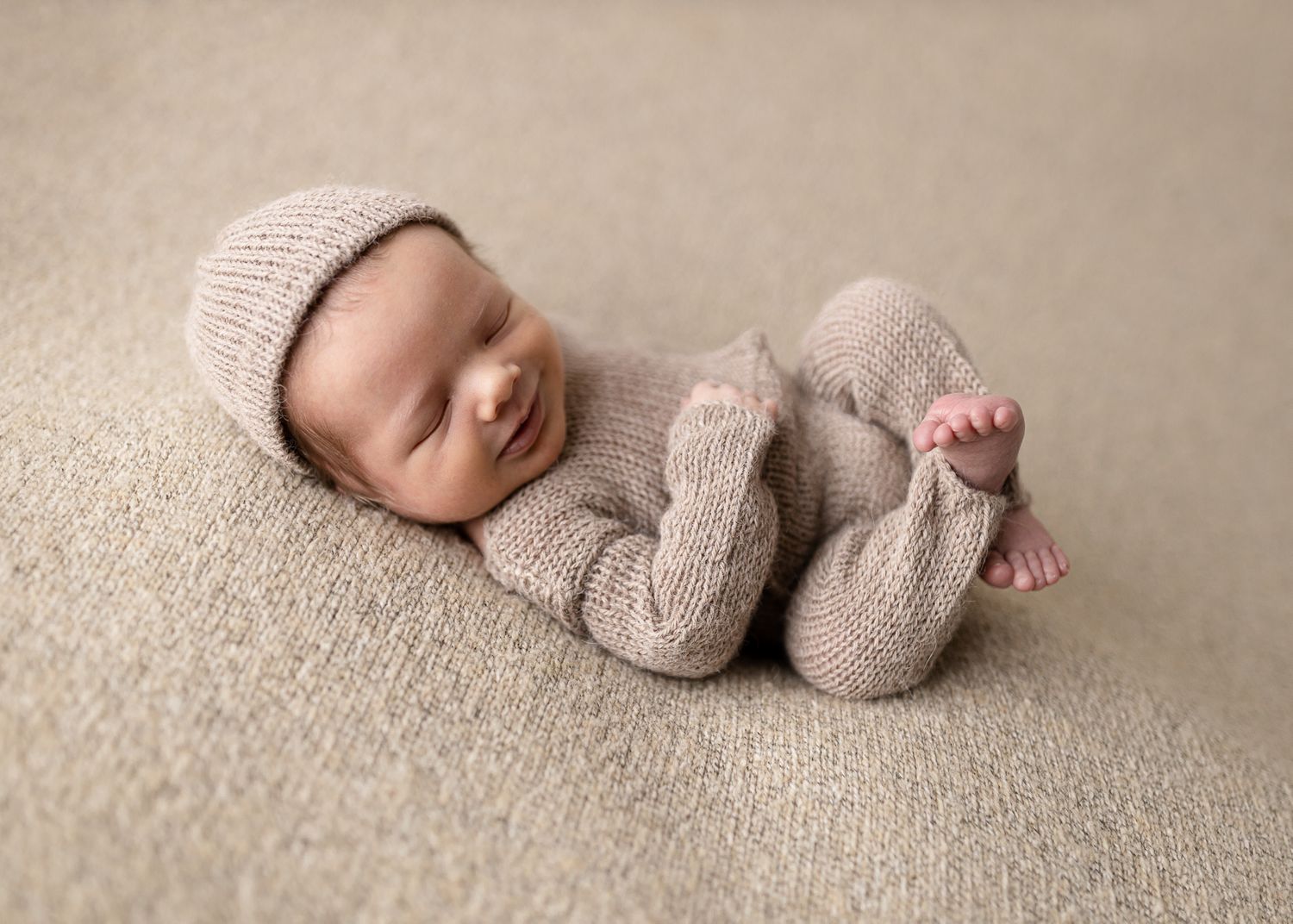 Sleeping newborn baby wearing soft knit clothing on beige carpet.
