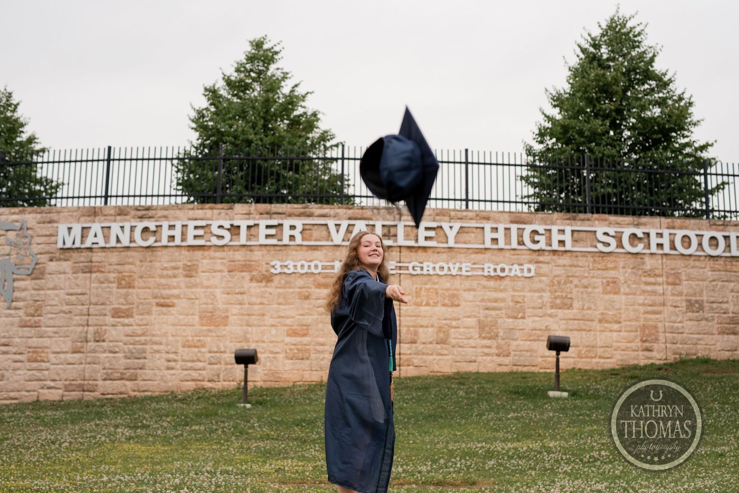 Graduate tosses cap in front of Manchester Valley High School stone entrance sign.