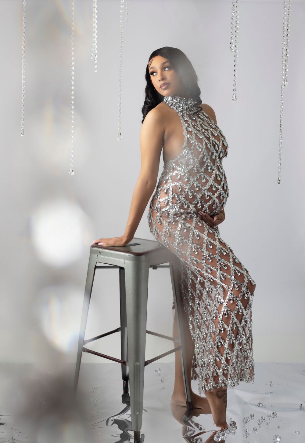 Maternity photos with crystal decorations and silver sequined dress against white background.