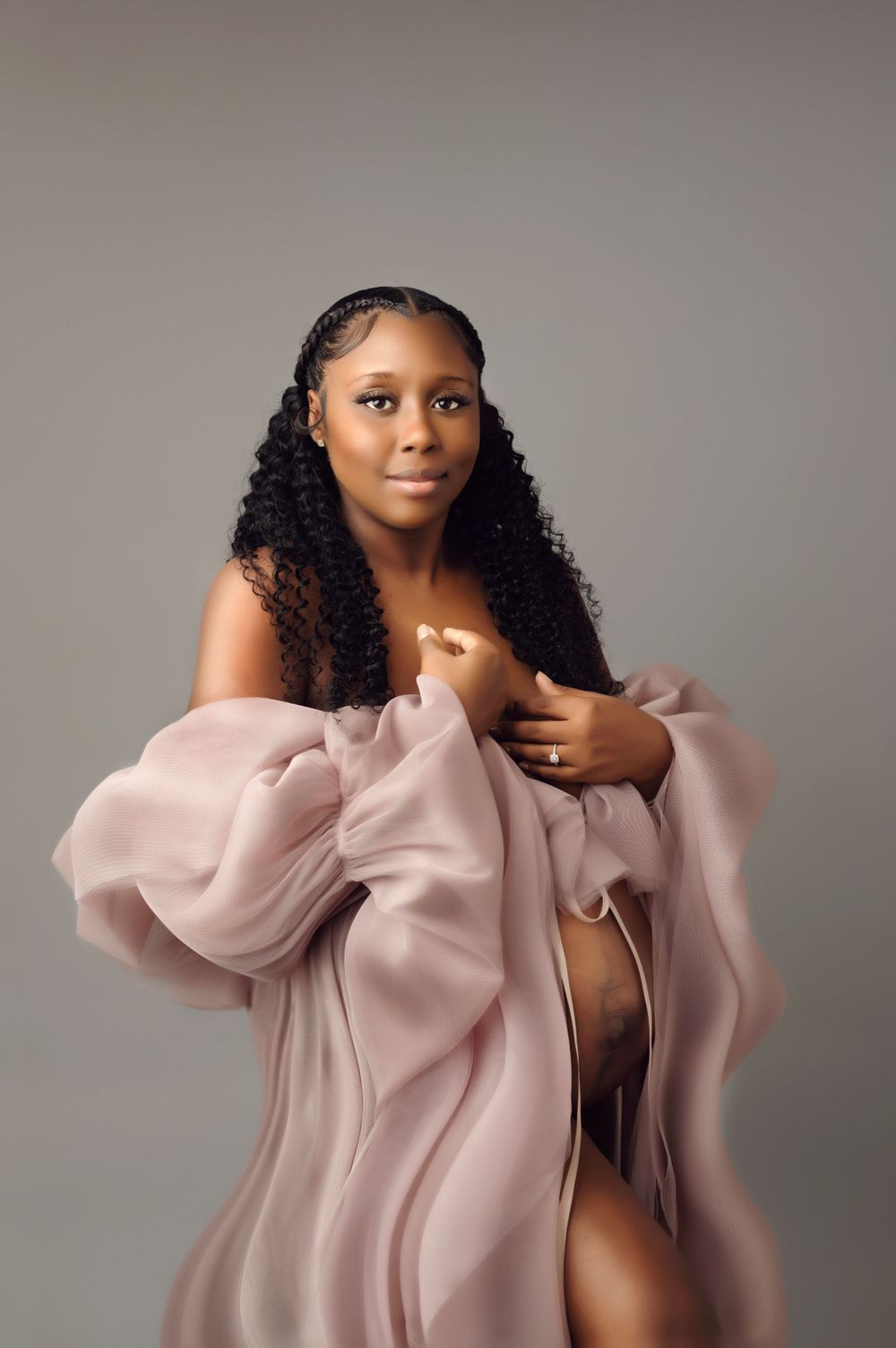 Intimate maternity portrait with soft pink flowing fabric against neutral backdrop.