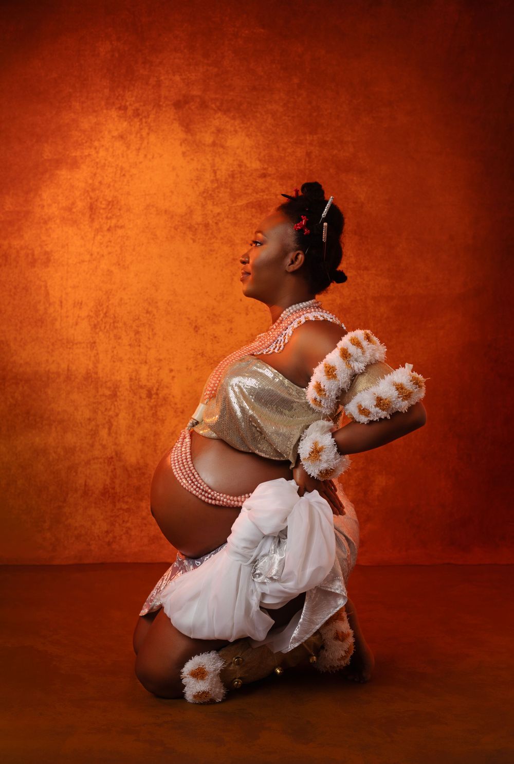 Artistic maternity photos with white floral accessories against warm orange backdrop.