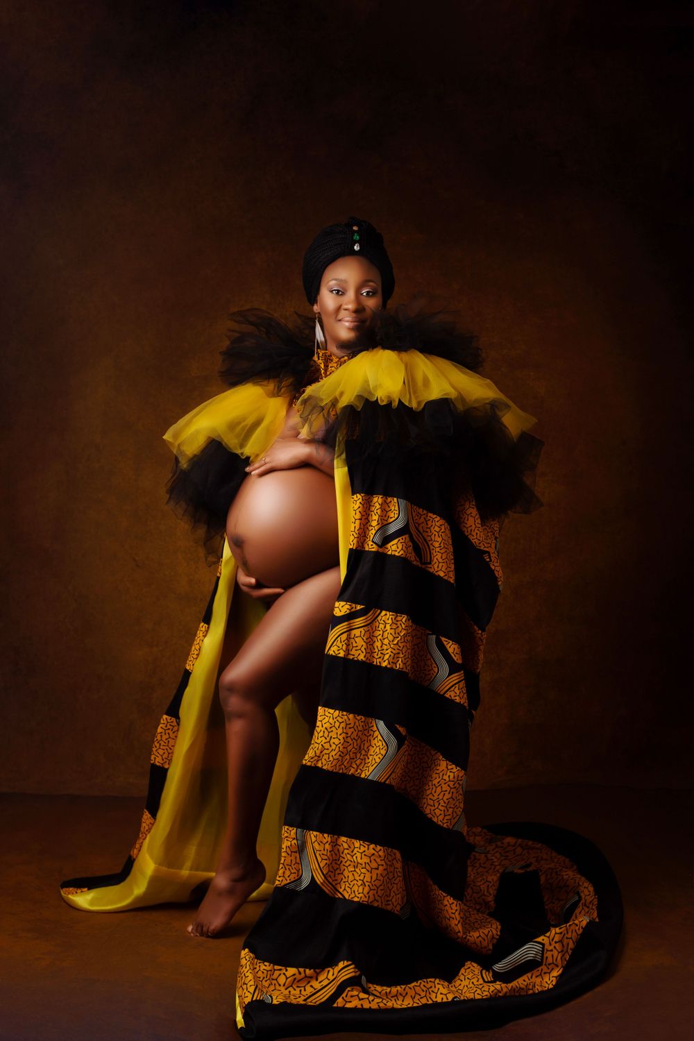 Maternity portrait with yellow and black patterned fabric in warm toned studio setting.