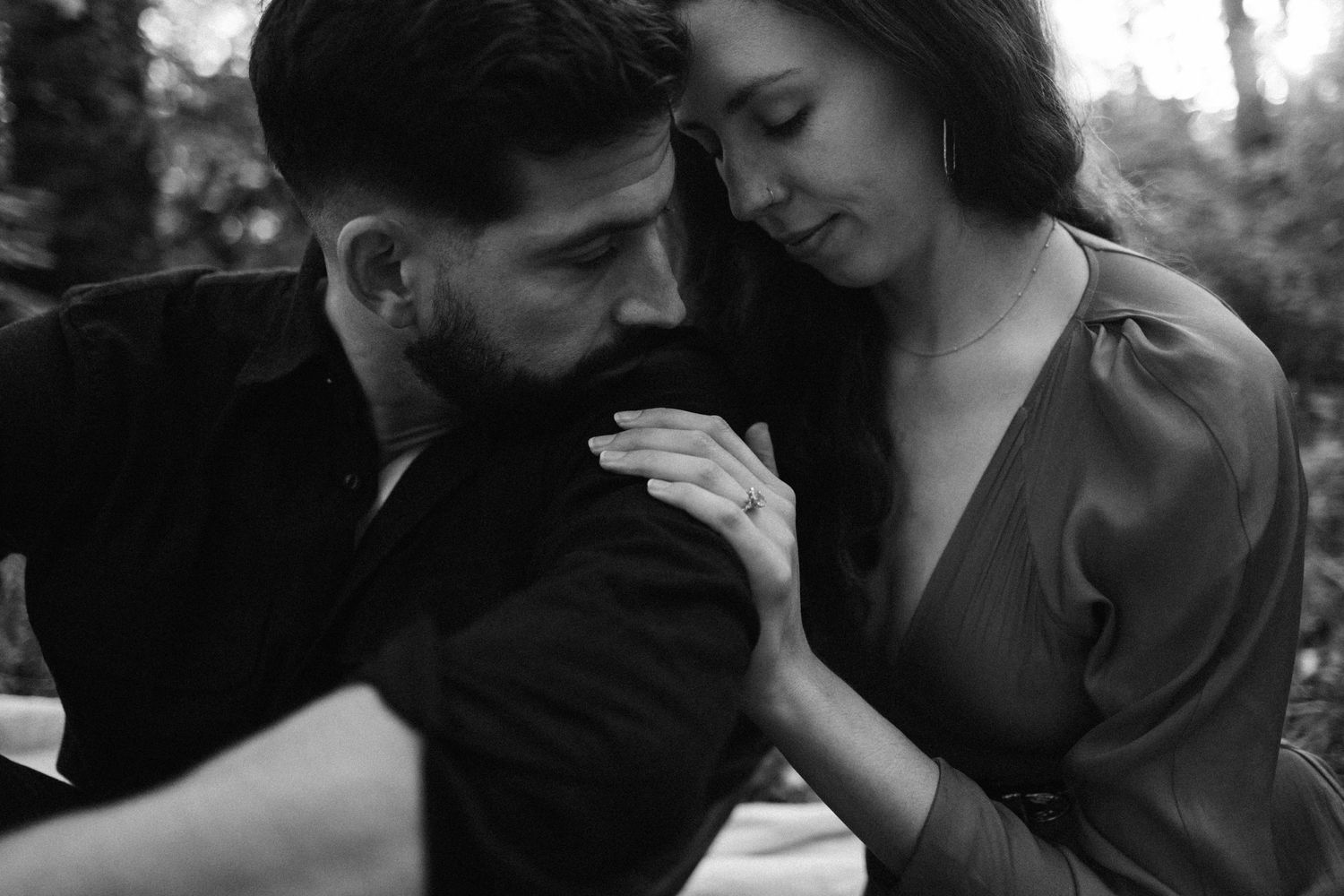 A romantic black and white portrait of a tender moment between a couple in an outdoor setting.