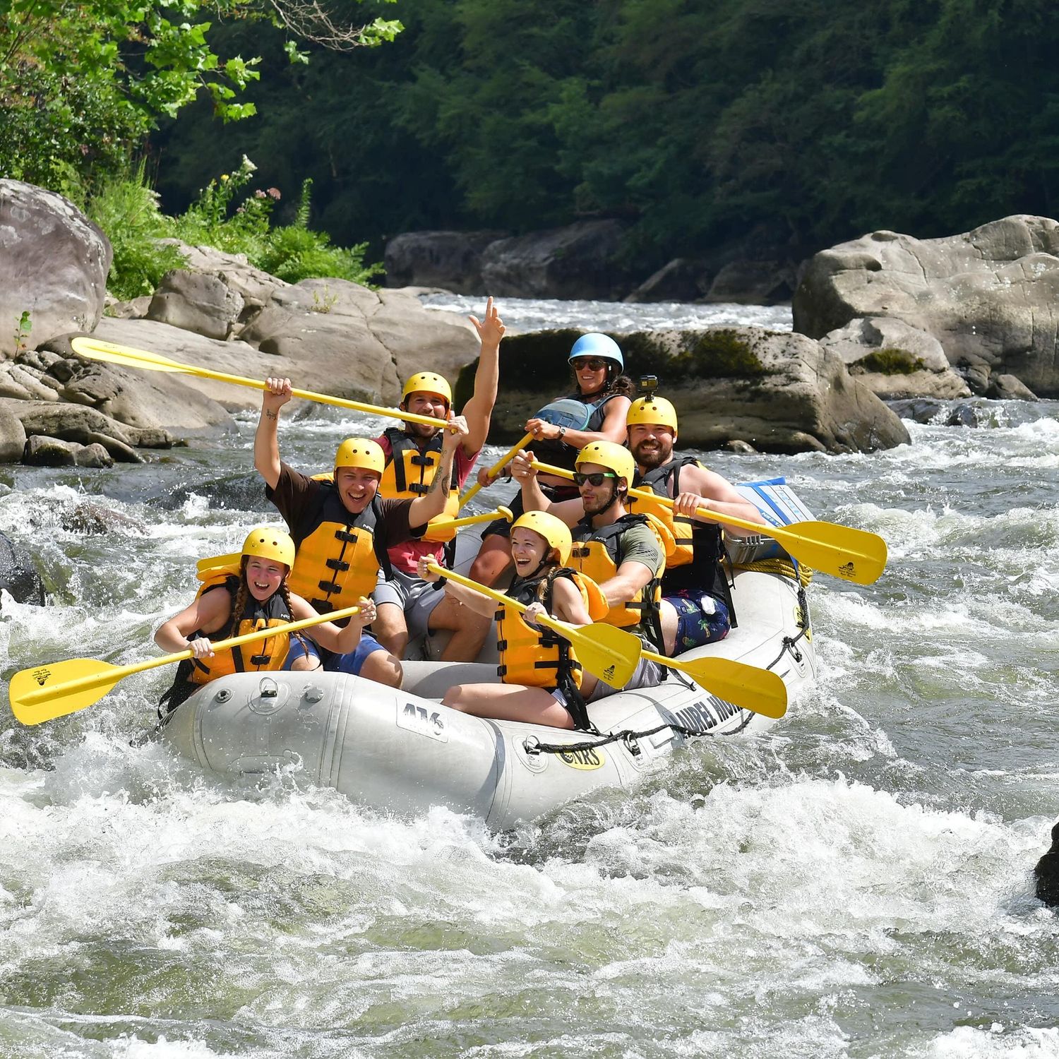 Group of adventurers white water rafting through rocky rapids while paddling and cheering.