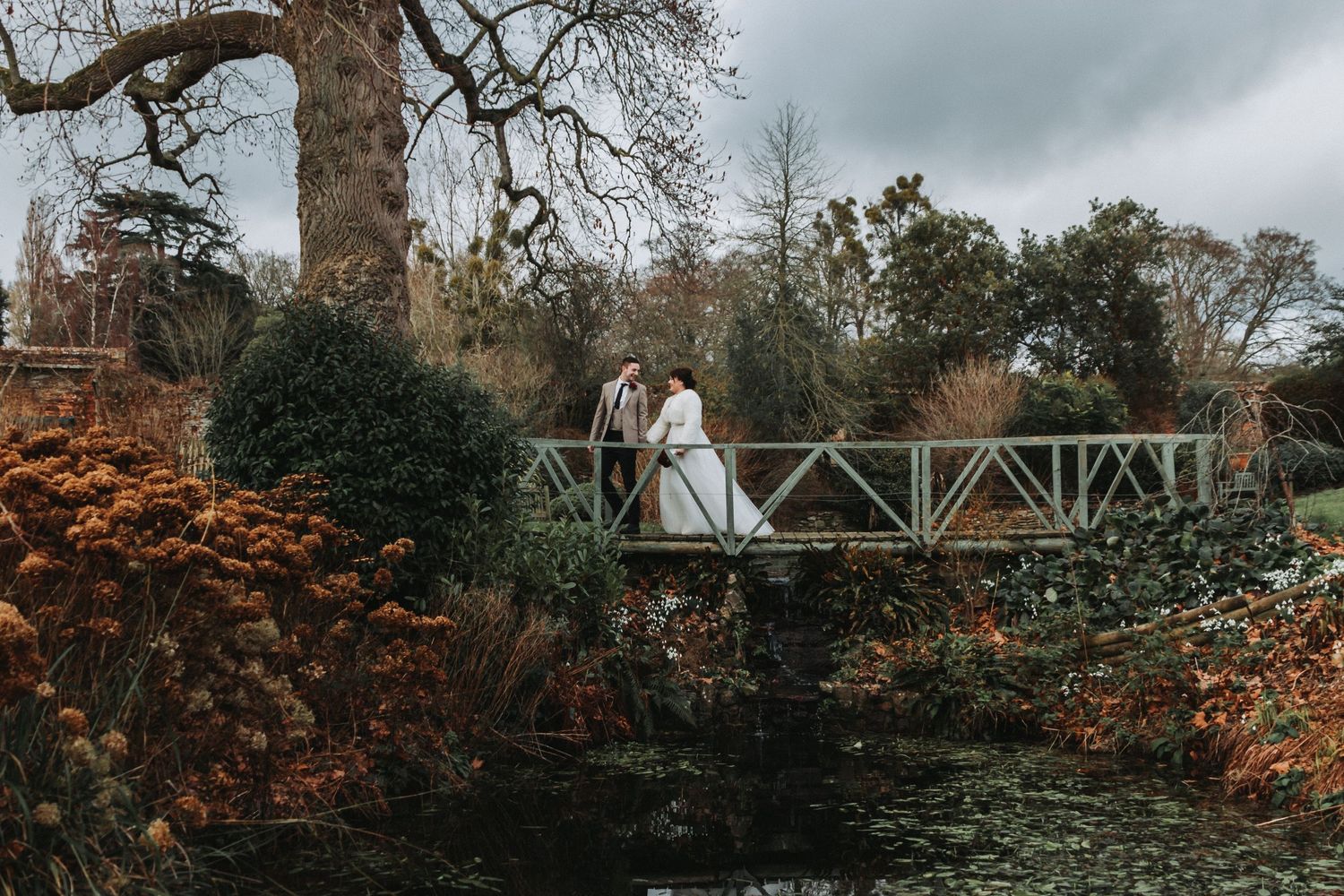 Couple in wedding attire walking across a bridge at their wedding venue