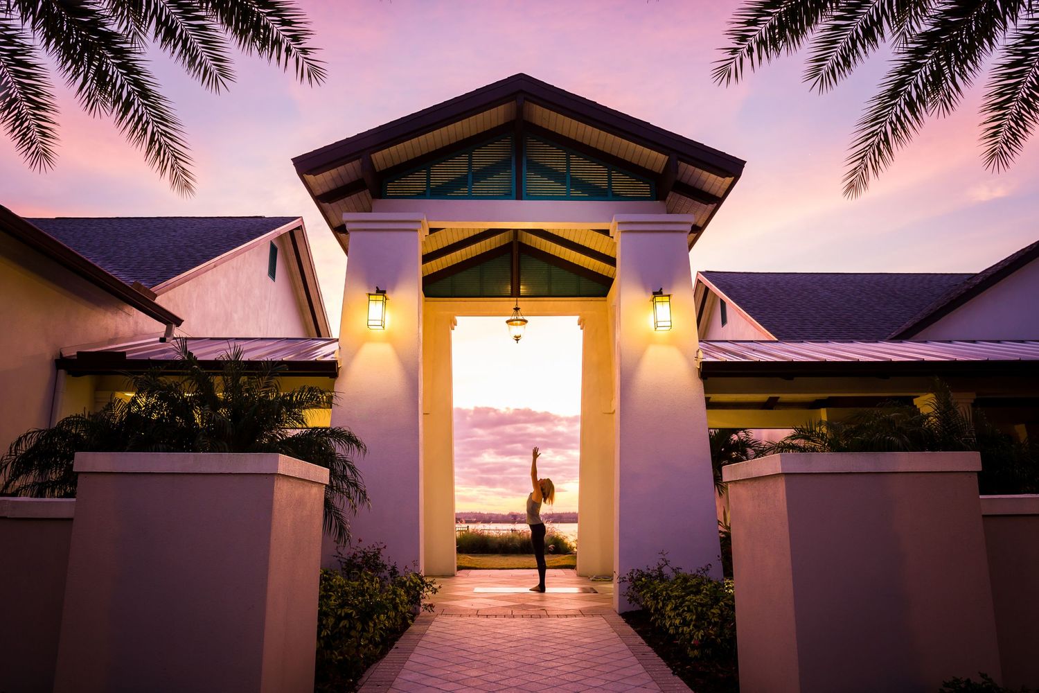 Stunning resort entrance at sunset with silhouette figure framed by glowing archway and tropical palm trees.