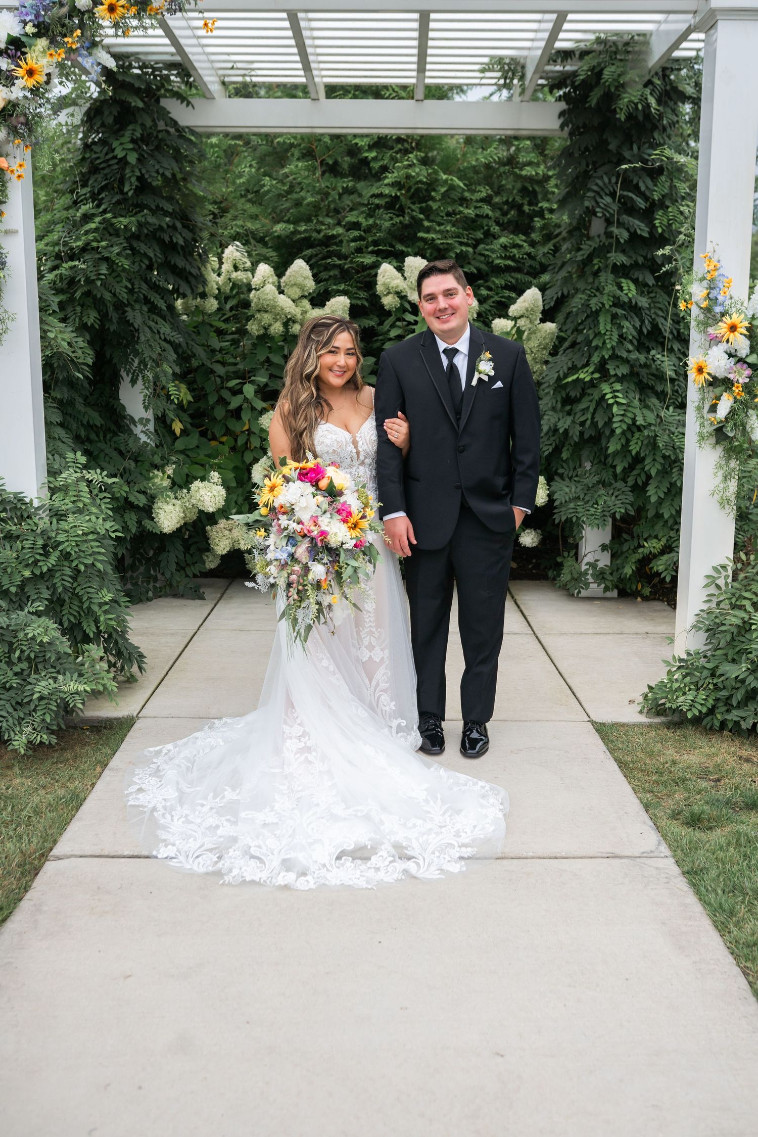 A bride and groom pose for a portrait together on their wedding day, surrounded by a lush garden.