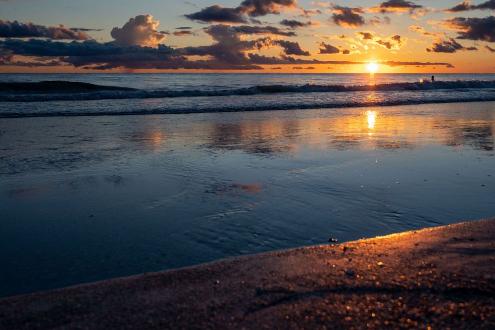Golden sunset reflects on wet sand beach as waves roll in during dusk.