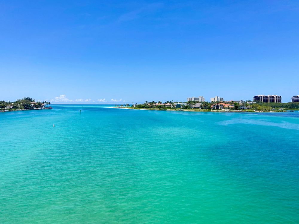 Aerial view of tropical turquoise waters and coastal buildings under bright blue sky.