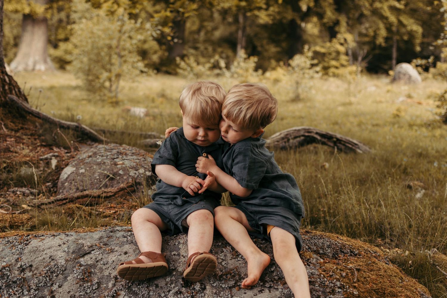 Two young children sit together on rocks in a rustic outdoor setting during golden hour.